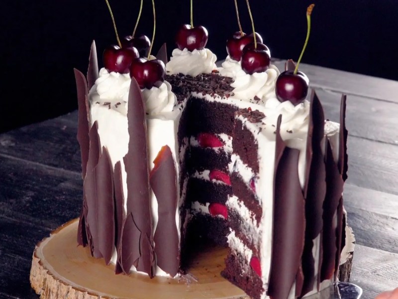 Eine Schwarzwälder Kirschtorte, aus der ein Stück Kuchen mit einem Tortenheber entnommen wird.