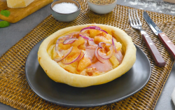 Ein Pizza Pot Pie mit Ananas und Schinken auf einem Teller. Daneben liegt Besteck.