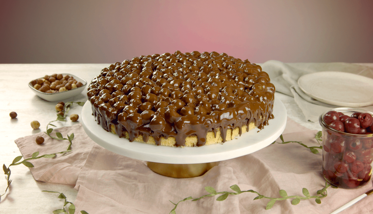 Ein Marmorkuchen mit Kirschen, Haselnüssen und Schokoglasur auf einer Tortenplatte.