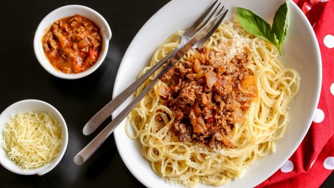 Teller mit One-Pot-Pasta à la bolognese auf holzigem Untergrund