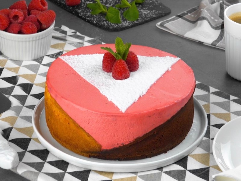 Schiefer Himbeerkuchen in geometrischem Design mit drei Farben, mit Himbeeren und Puderzucker sowie Minze dekoriert.