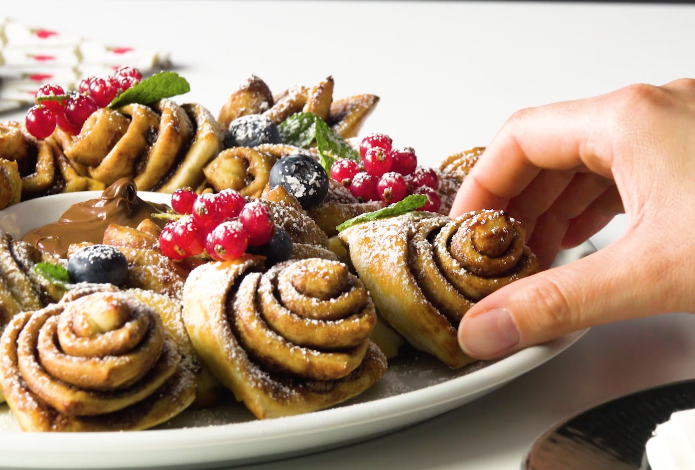 Eine Hand greift nach einem StÃ¼ck des mit Puderzucker bestreuten Nutella-Kranzes.