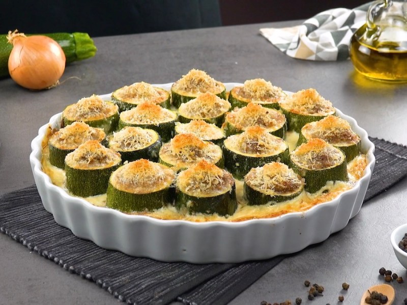 Eine runde Auflaufform mit gefüllten Zucchini-Happen, mit Käse bestreut.