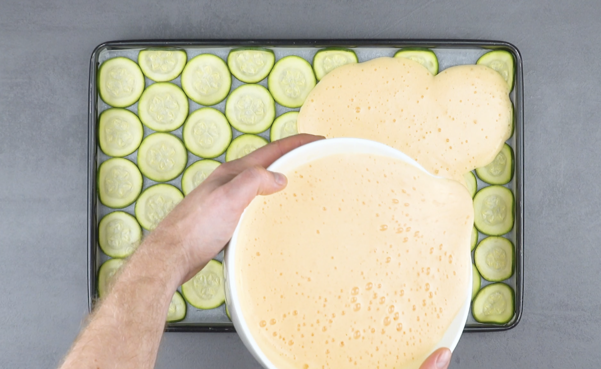 Das verquirlte Ei wird Ã¼ber die Zucchinischeiben auf Backblech verteilt