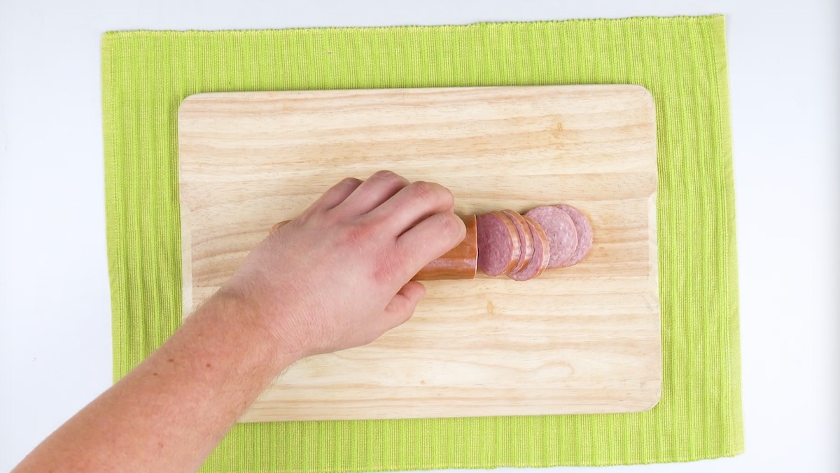 5 Scheiben werden von Wurst auf Holzbrett abgeschnitten