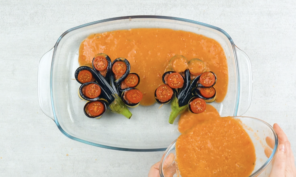 2 gefÃ¼llte Auberginen in Blumenform in einer Auflaufform, in die TomatensoÃŸe gegossen wird