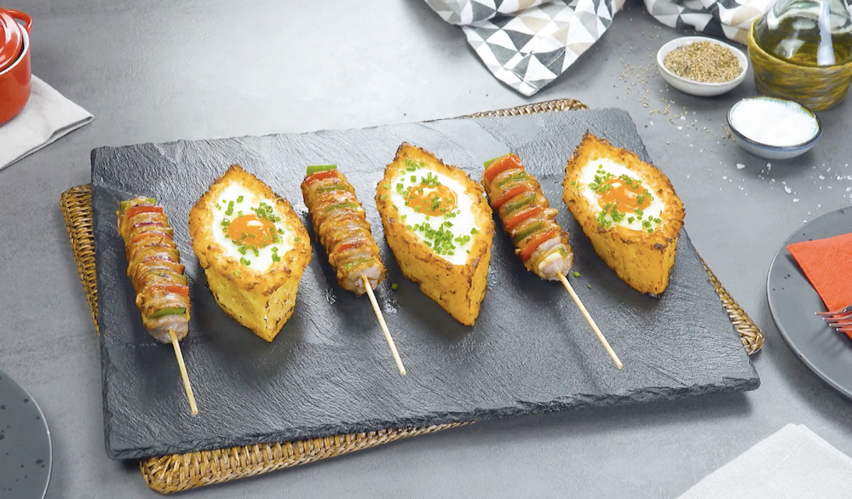 Hasselback-BratwÃ¼rste und Kartoffelboote mit Ei nebeneinander auf Schieferplatte