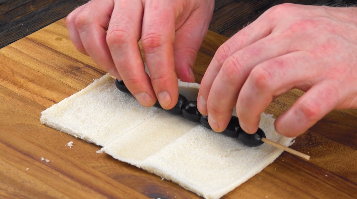 Oliven am SpieÃŸ werden in Toastbrotscheiben eingerollt