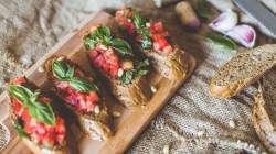 4 kleine Brote mit Bruschetta Italiana auf einem Holzbrett. Daneben liegen Brotscheiben.