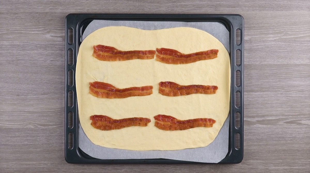 6 Baconscheiben werden auf Pizzateig auf mit Bsckpapier belegtem Backblech gelegt