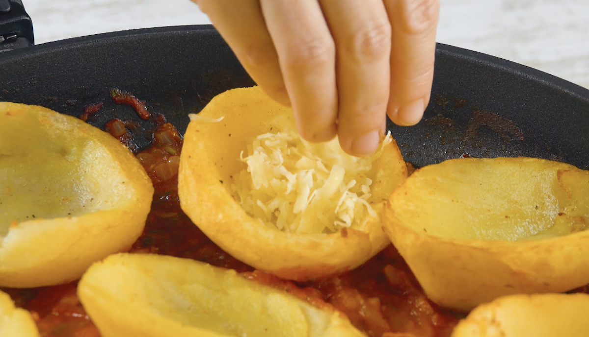 Geriebener KÃ¤se wird in ausgehÃ¶hlte Kartoffeln in Pfanne gestreut