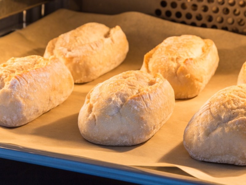 Brötchen auf einem mit Backpapier belegten Backblech im Ofen.