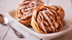 Mehrere Apfel-Zimtschnecken mit Walnüssen auf einem Teller. Daneben liegt ein Löffel.