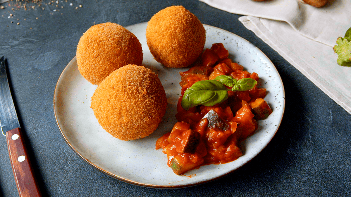 Drei Arancini liegen zusammen mit TomatensoÃŸe servierfertig auf einem weiÃŸen Teller.