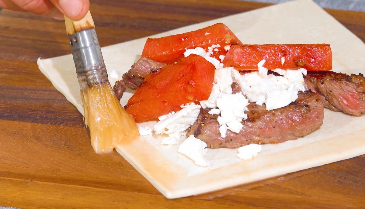 BlÃ¤tterteig-Quadrat wird mit Melon, Feta udn Rumpsteak belegt und Rand mit Ei bestrichen