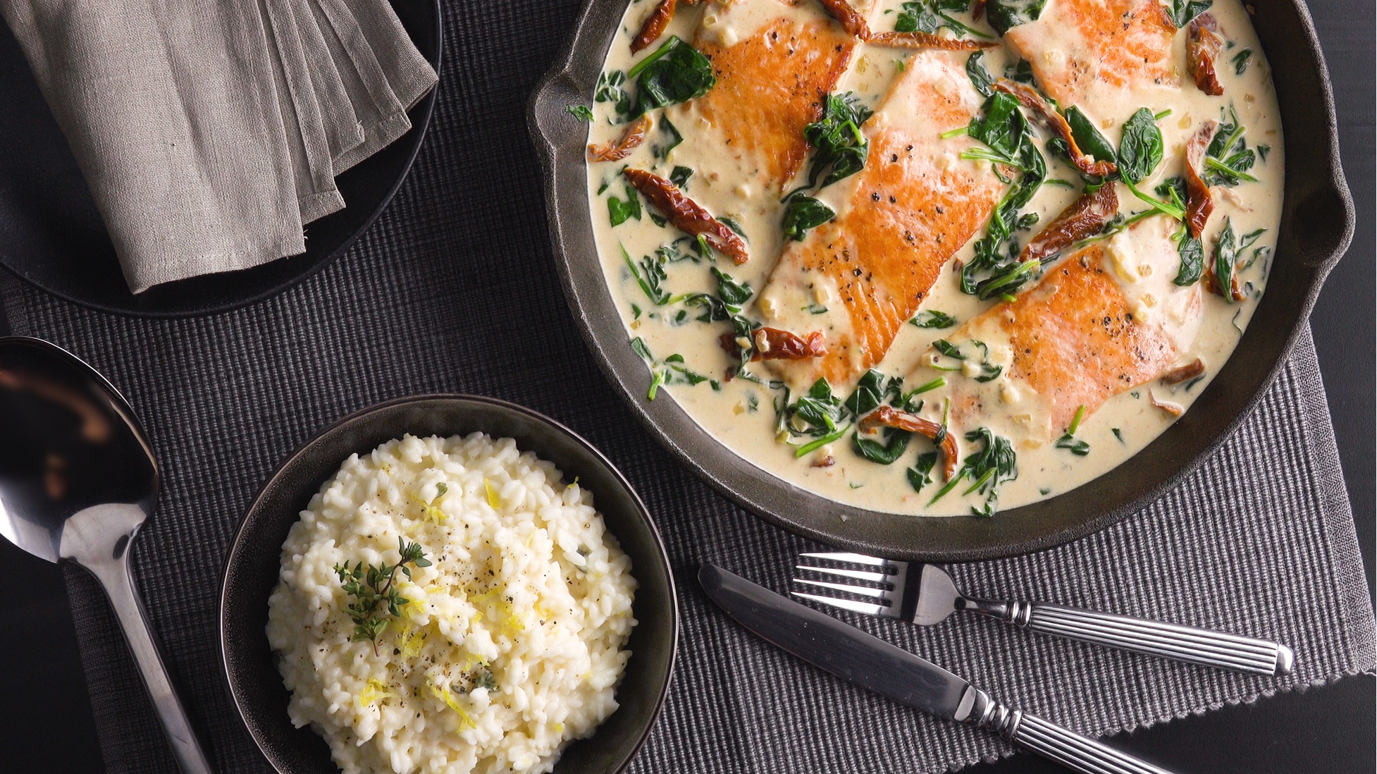 Lachs-Pfanne mit getrockneten Tomaten und Spinat, daneben eine Schale mit Zitronenrisotto