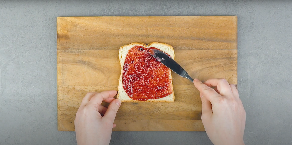 Eine Toastscheibe wird mit Himbeermarmelade bestrichen. 