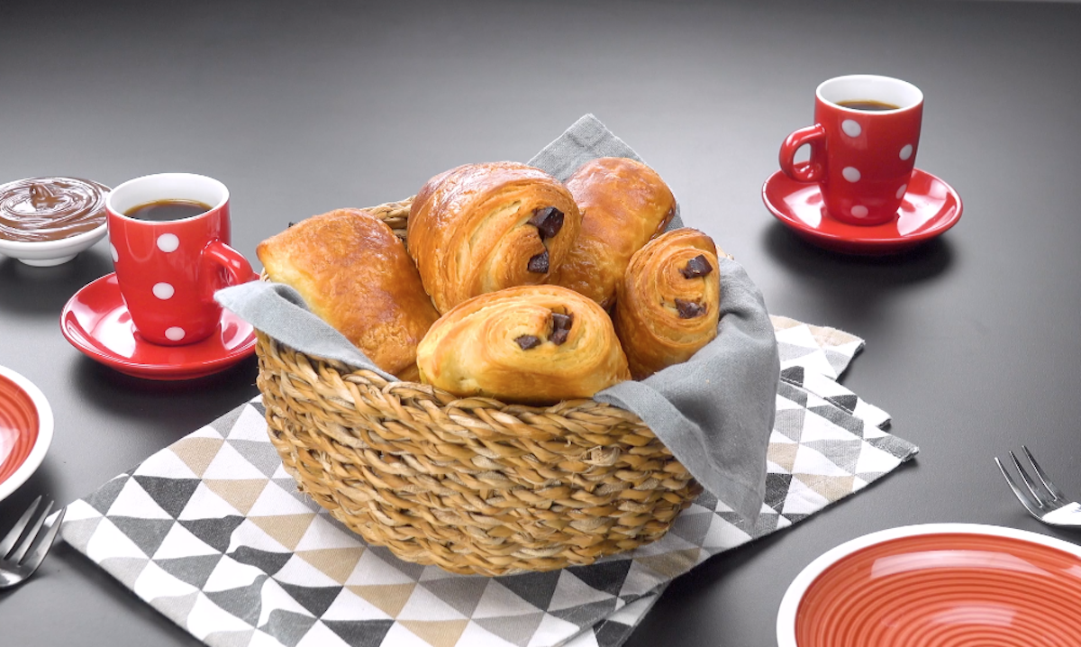 Ein Korb voller Pain au chocolat mit Kaffeetassen im Hintergrund