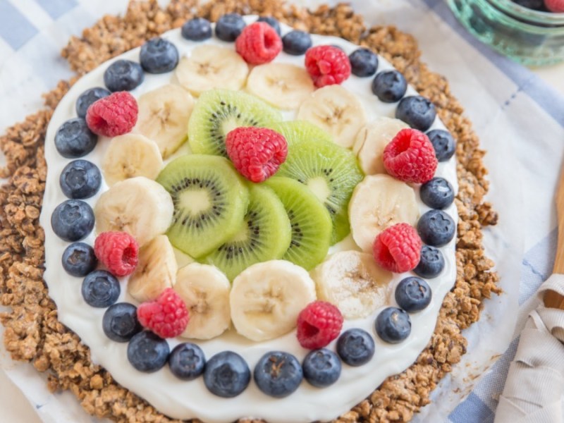 Frühstückspizza aus Haferflocken mit Joghurt und frischem Obst. Daneben liegt Besteck.