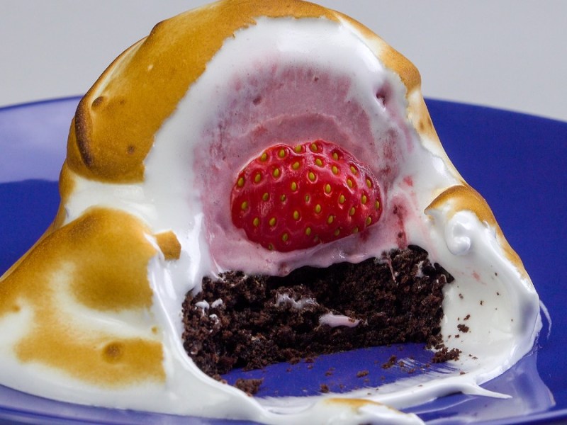 Gebackenes Eis mit Erdbeeren und Baiserhaube auf Teller, das angeschnitten wurde.