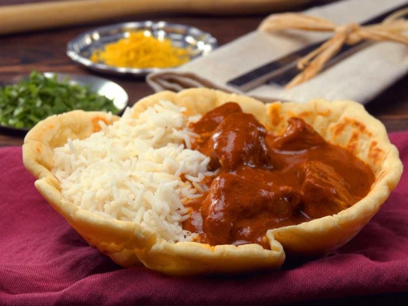 Eine Portion Hähnchencurry mit Reis in Schale aus Naan-Brot.