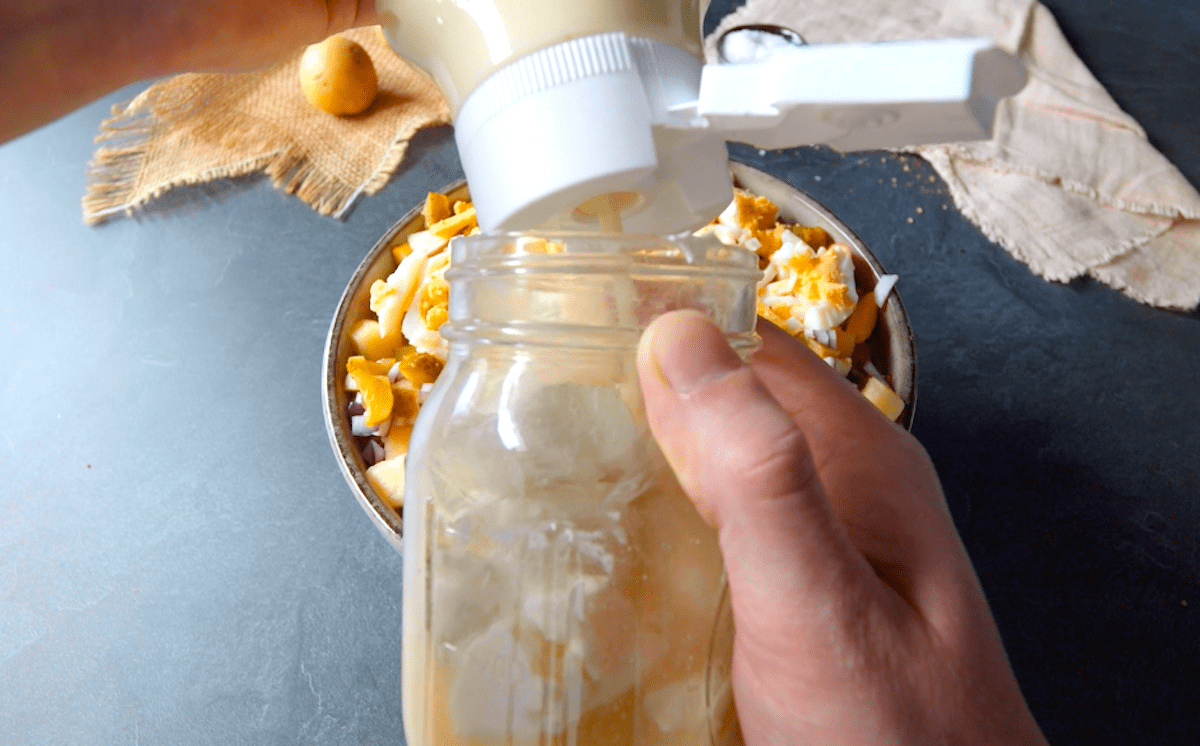 Mayonnaise wird zu FrischkÃ¤se und GewÃ¼rzgurkenwasser in ein Glas hinzugegeben.