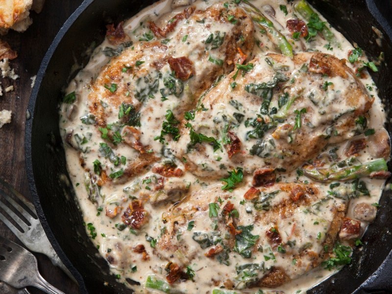 Hähnchen in Parmesan-Soße in einer Pfanne, von oben fotografiert. Daneben liegen Besteck und Brotstücke.