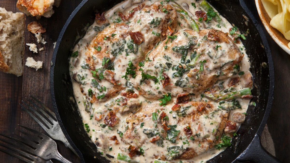 Hähnchen in Parmesan-Soße in einer Pfanne, von oben fotografiert. Daneben liegen Besteck und Brotstücke.