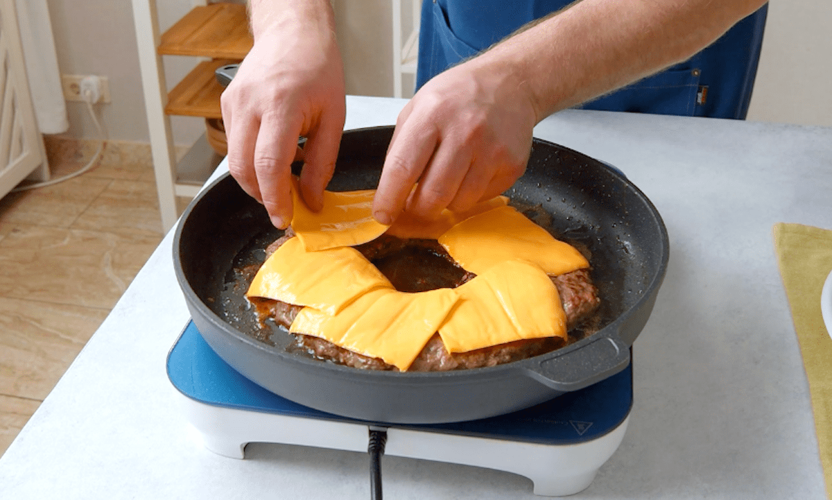 Cheddar wird auf ein Burger Patty in der Pfanne gelegt