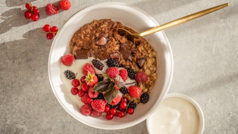 Schokoladen-Porridge in weißer Schüssel mit Obst, Draufsicht.