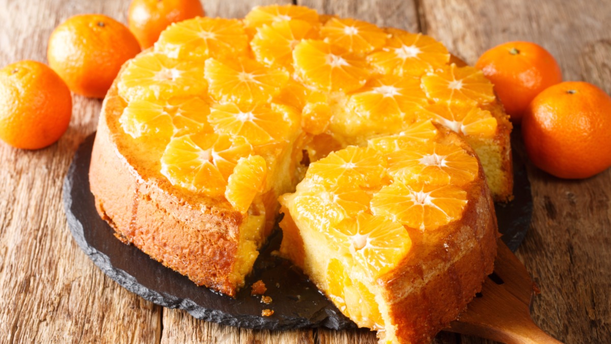 Ein Schüttelkuchen mit Mandarine. Ein großes Stück wurde herausgeschnitten und liegt vor dem Kuchen.