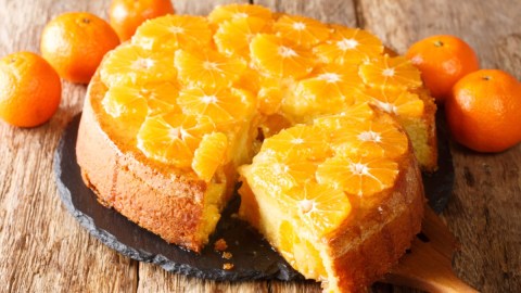 Ein Schüttelkuchen mit Mandarine. Ein großes Stück wurde herausgeschnitten und liegt vor dem Kuchen.