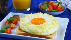 Ein fluffiges Wolkenei auf Toast mit aufgeschnittenen Tomaten auf einem Teller.