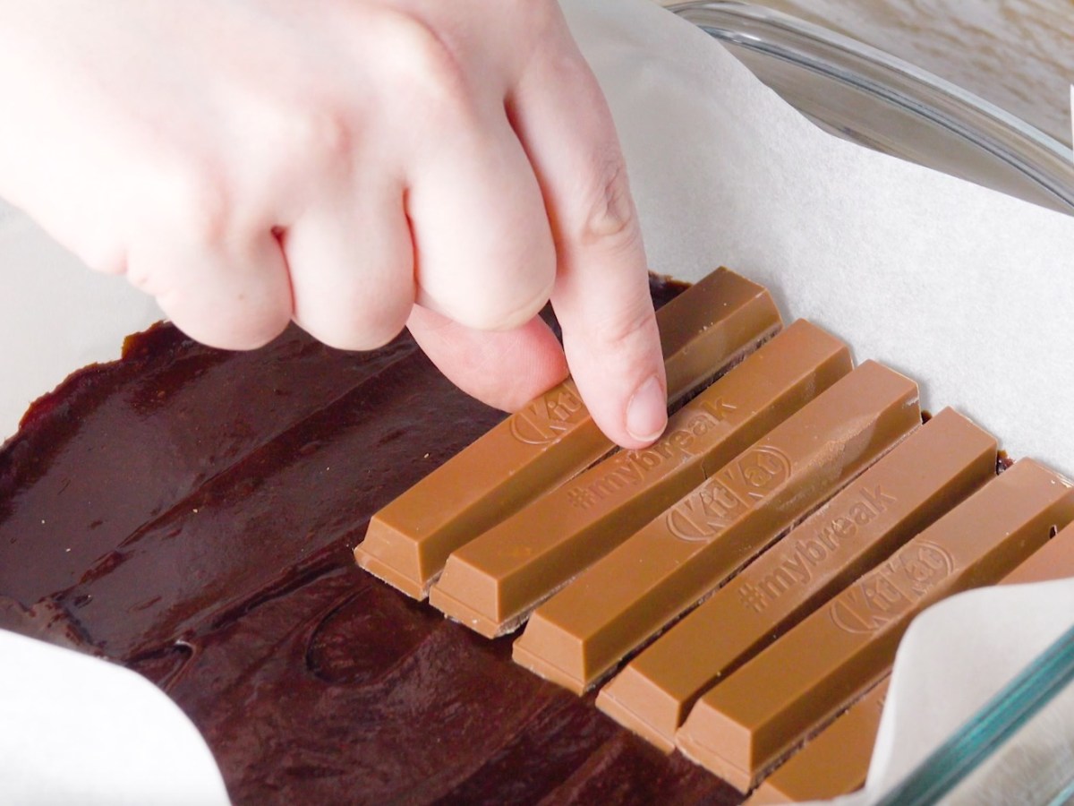 Ein noch ungebackener Kit-Kat-Kuchen in der Auflaufform, auf den gerade Schokoriegel gelegt werden.