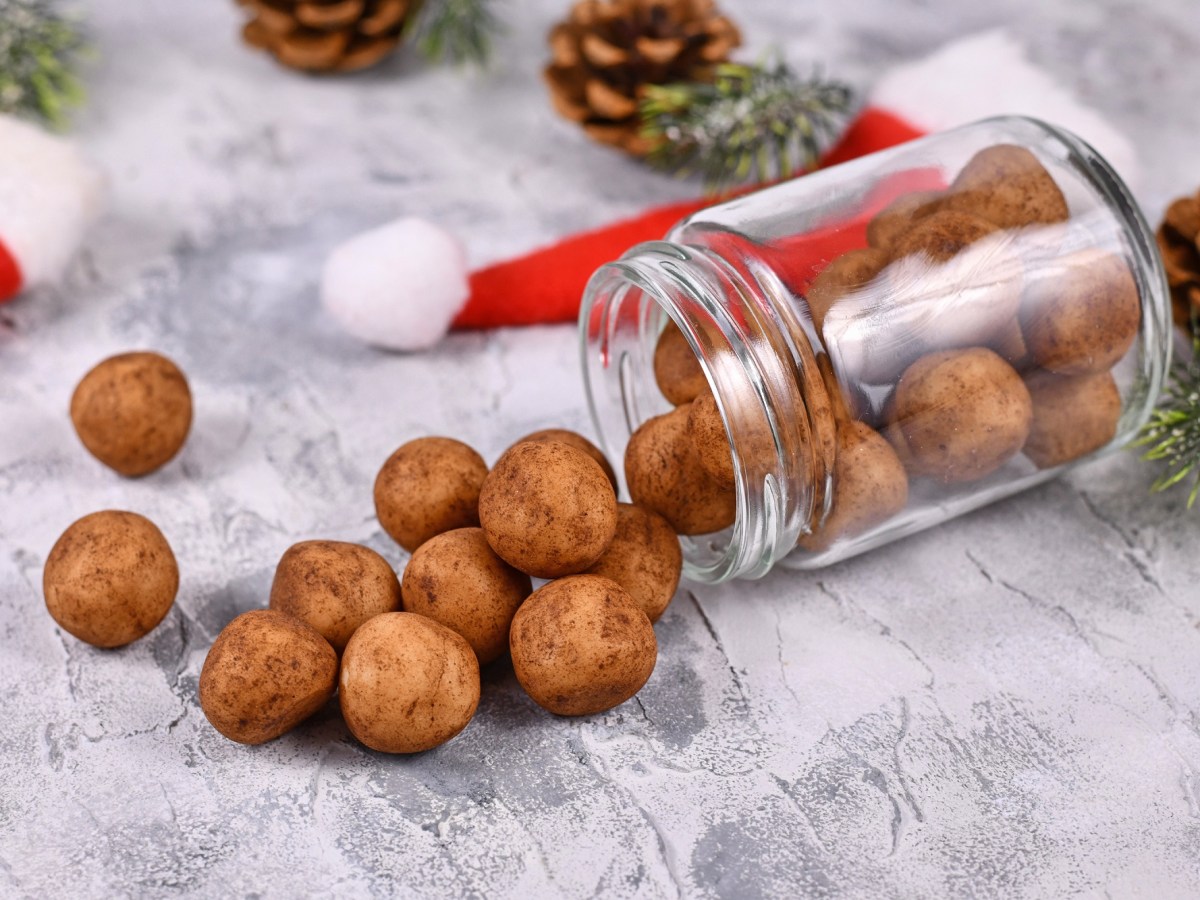 Ein umgekipptes Glas Marzipankartoffeln, drumherum Tannenzapfen und kleine Weihnachtsmützen.