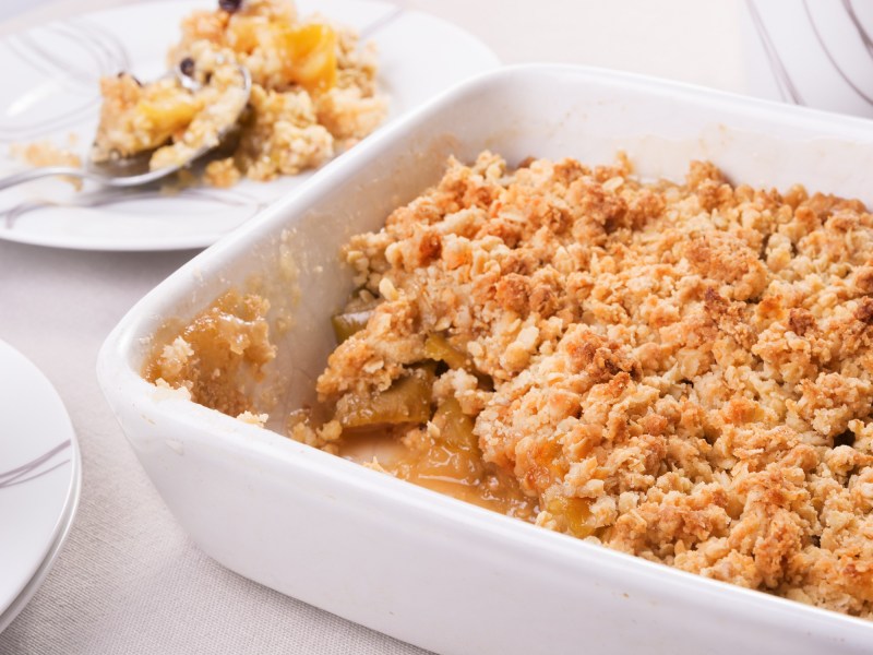 Eine Auflaufform mit Quitten-Crumble, von der schon eine Portion abgenommen wurde und auf einem Teller dahinter liegt.