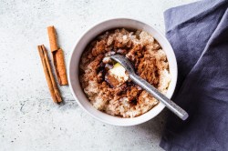 Eine Schüssel Spekulatius-Porridge mit einem Löffel, daneben Zimtstangen und eine blaue Serviette aus Stoff, alles Draufsicht.