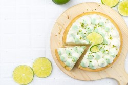 Gin-Tonic-Kuchen in der Draufsicht, auf einem Brett, ein Stück ist schon angeschnitten, verziert mit Limetten.