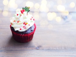 Ein Glühwein-Cupcake mit Zuckerperlen verziert, im Hintergrund unscharf Lichterketten.