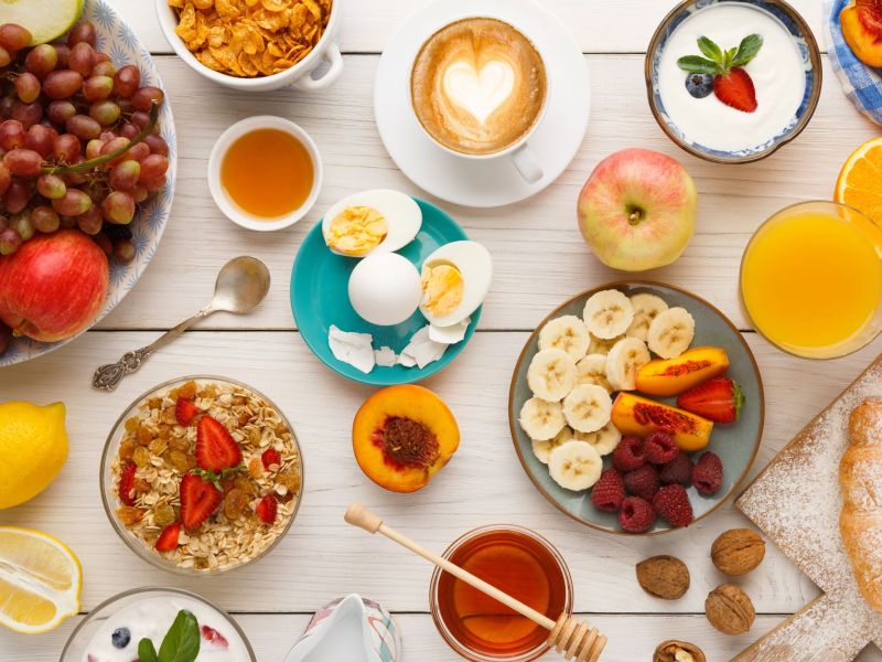 Ein bunt gedeckter Frühstückstisch mit Obst, Müsli, Eiern, Kaffee und Saft.