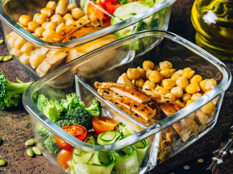 2 Glascontainer mit gesundem, vorbereiteten Essen. Daneben eine Gabel und eine kleine Glaskaraffe mit Öl.