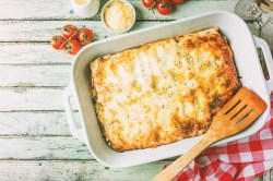 Sauerkraut-Lasagne in Auflaufform, darauf ein Holzlöffel, drumherum Tomaten und Käse, Draufsicht.