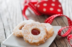 3 Spitzbuben-Plätzchen auf einem Teller, daneben weihnachtliches rotes Geschenkband.