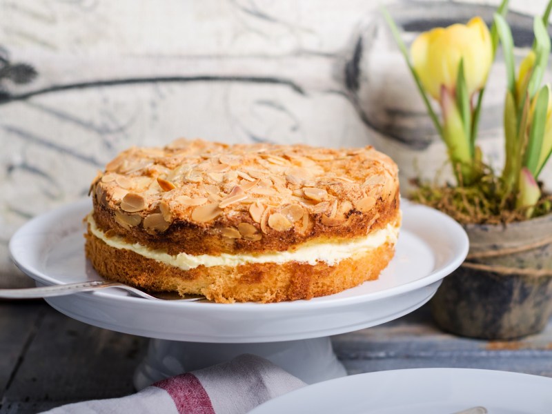 Ein Bienenstich-Kuchen auf einer Tortenplanne, daneben frische Tulpen.