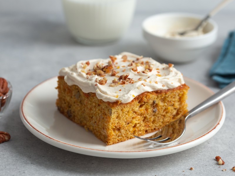 Ein viereckiges Stück Carrot Cake mit Frischkäse-Frosting auf einem weißen Teller