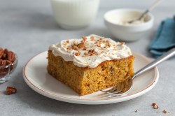 Ein viereckiges Stück Carrot Cake mit Frischkäse-Frosting auf einem weißen Teller