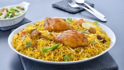 Ein tiefer Teller mit Chicken Biryani. Im hintergrund sind Besteck und eine Schale mit Salat.