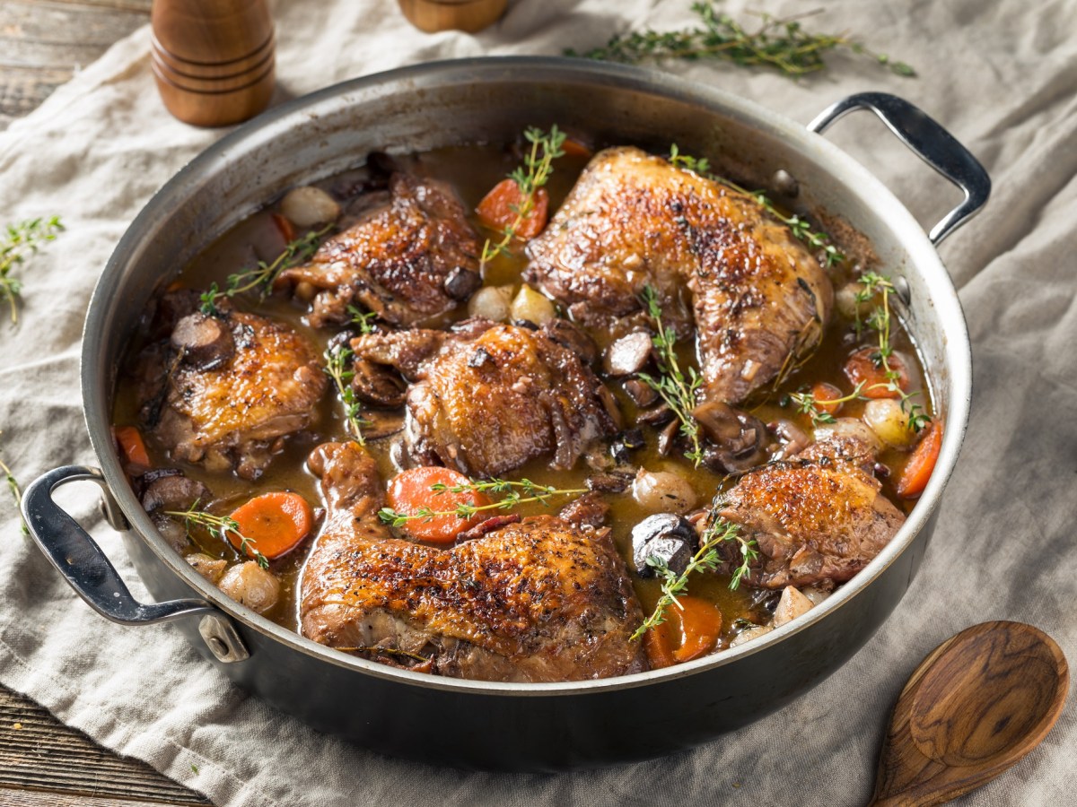 Coq au Vin mit Thymian garniert in einer gusseisernen Pfanne auf einem grauen tuch.