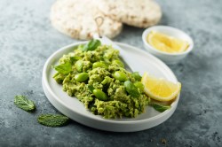 Edamame-Guacamole, mit etwas Minze garniert, auf einem weißen Teller. Serviert mit Pita-Brot.