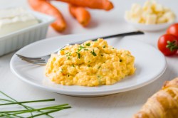 Ein Teller französisches Rührei garniert mit Kräutern, darauf auch eine Gabel, drumherum verschiedene Zutaten wie Gemüse und Butter.